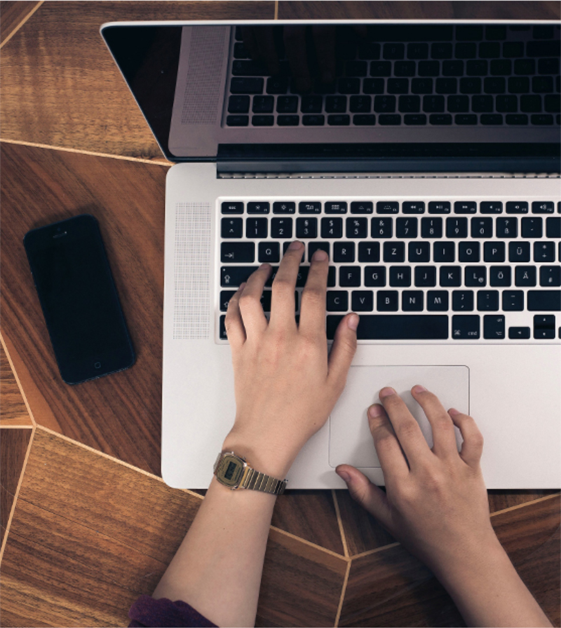 Image of overhead view of hands typing on a laptop