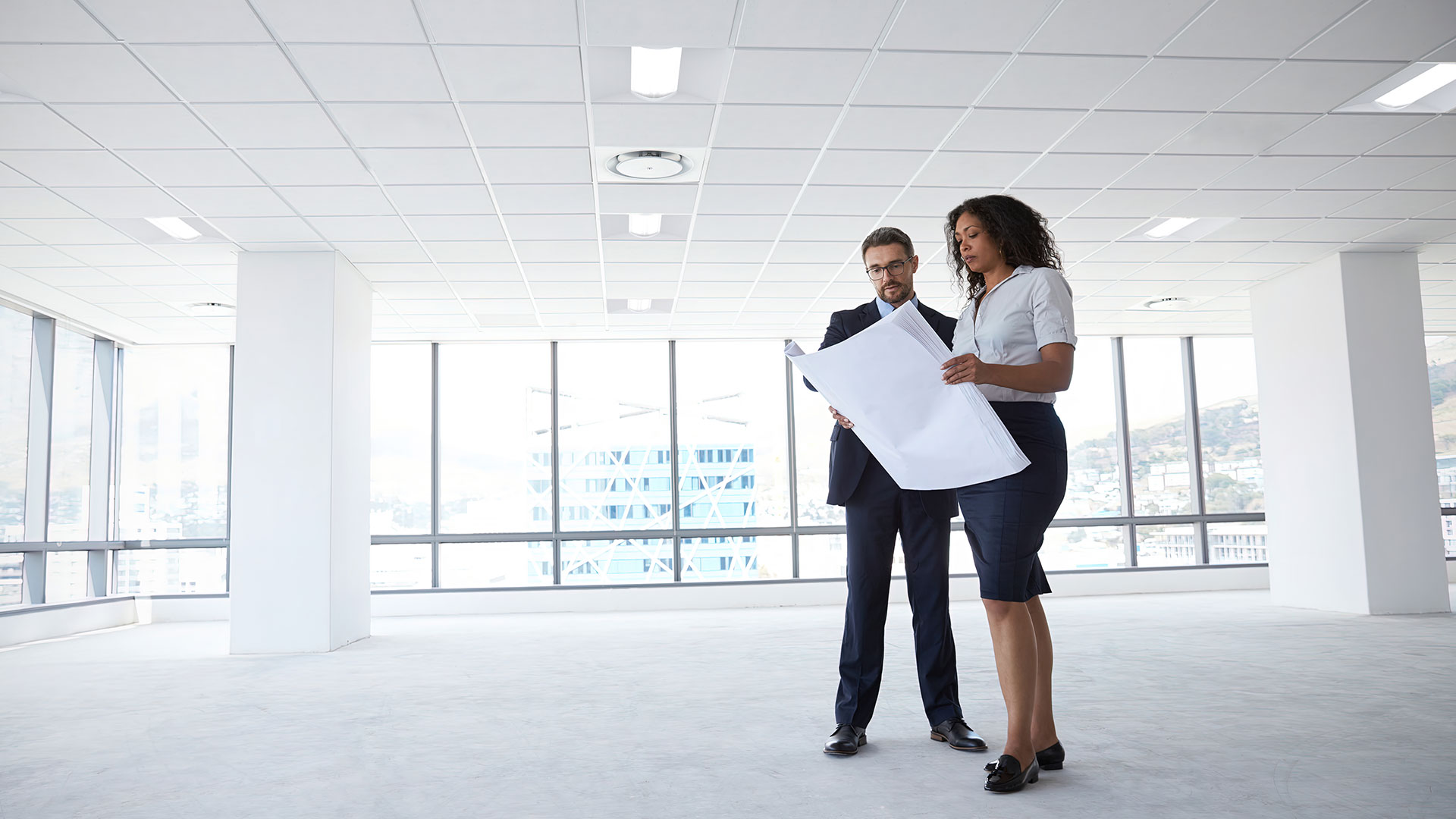 Business partners review plans for office space lit by center-element LED lay-in luminaires.