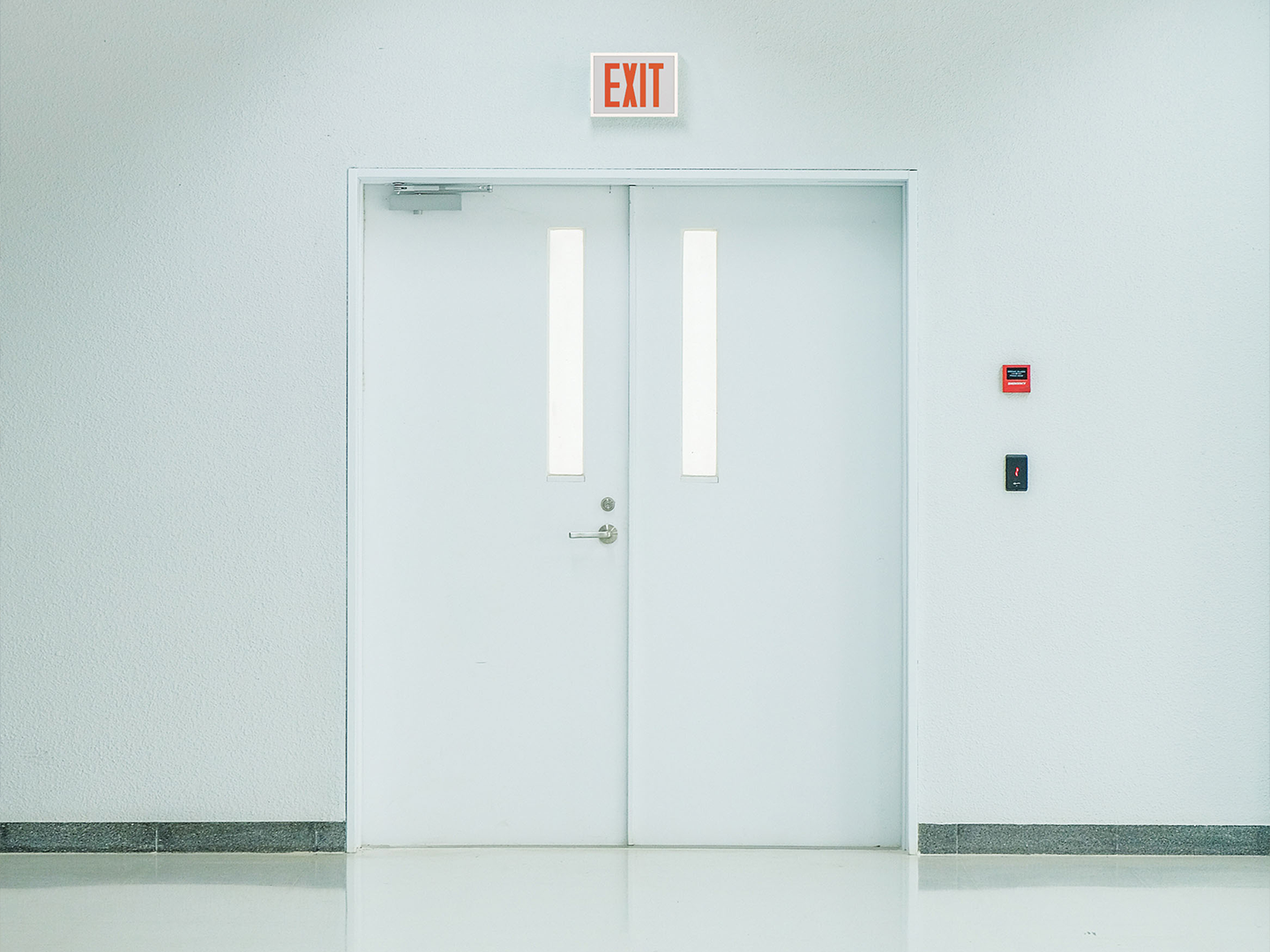 An exit sign from the Lithonia Titan Steel family is shown mounted above a door.