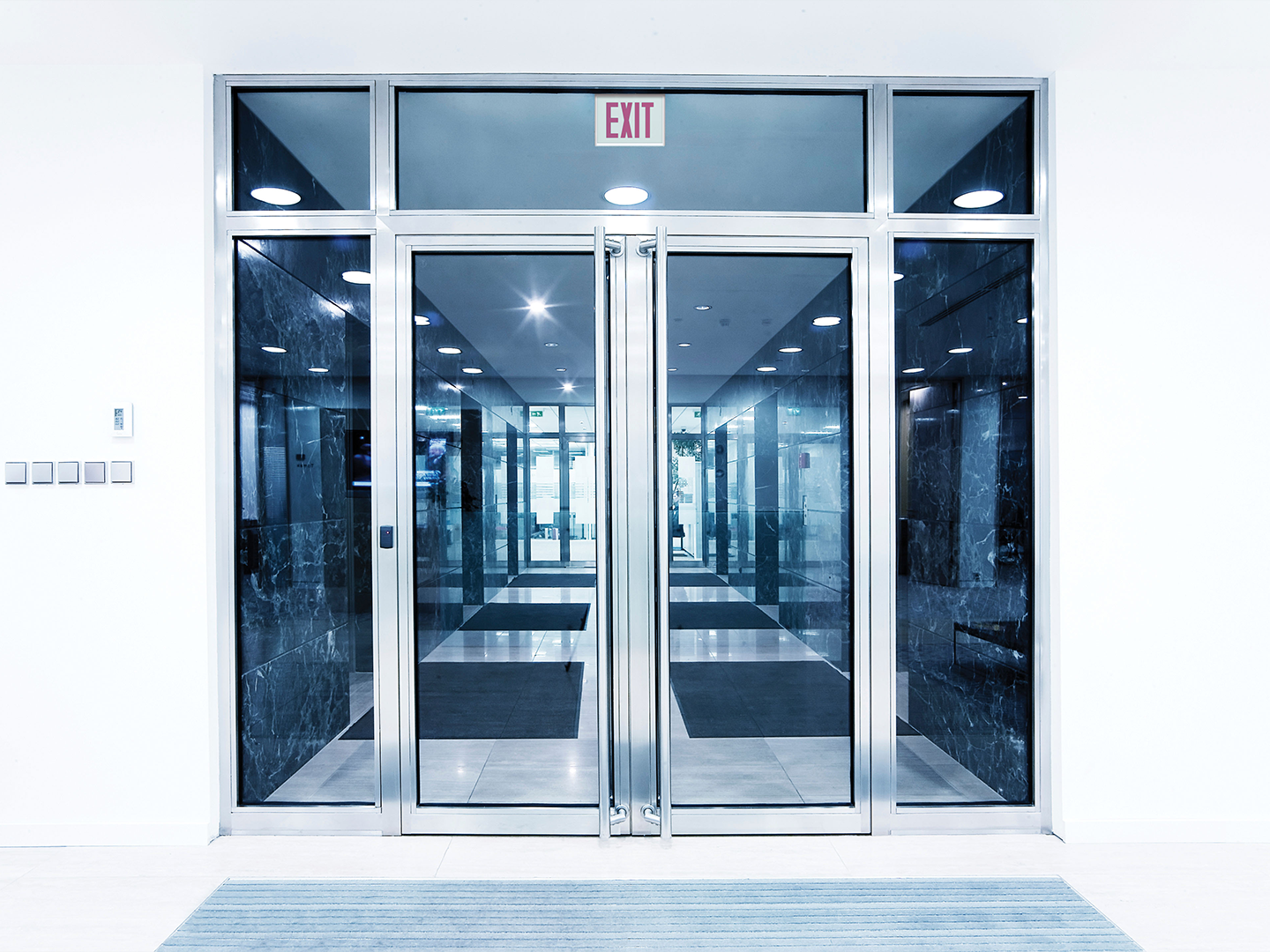A Lithonia Titan Steel exit sign is shown through the doors of a lobby.